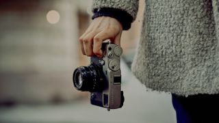 Best retro cameras: Person holding a Fujifilm X-Pro3 by the fingertips while walking